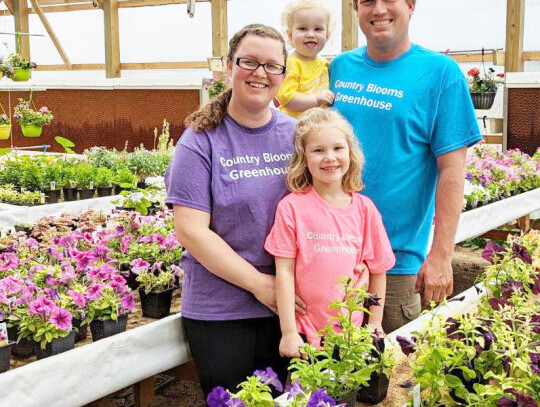 The Schmit family, Brooke, almost 2-year-old Audrey, Tim, and 5-year-old Natalie stand in their new greenhouse for their business, Country Blooms, in Randolph. More than 90 varieties of vegetables and flowers are laid out in colorful rows on flood tables,