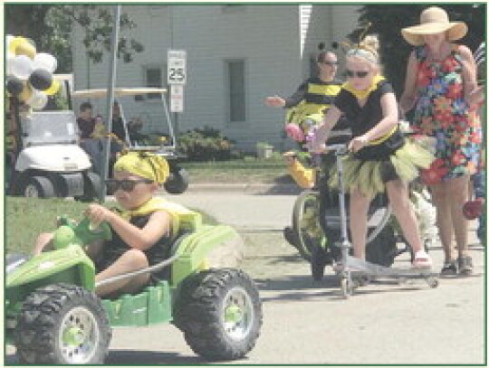 Braxton Dorcey shows off his cool ride during the Buzzin’ Around Randolph Bike Roll &amp; Stroll Sunday. Participants on bike, scooter, foot and golf cart traveled several blocks, many in costume. At left, Justin Guenther paints the black bee outline on