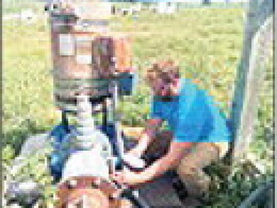 Assistant Manager Myles Lammers collecting a water sample from an irrigation well.