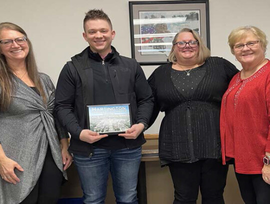 Hartington Chamber of Commerce President Karen Flamig presents Brett Klug, Christina Archer and Lynnette Krei with a plaque honoring the 25th anniversary of Farm Bureau Insurance’s Hartington office.