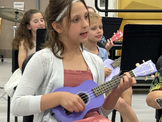 Jackie Loberg|Randolph Times Third grader Taylor Tjaden (above) strums the ukulele to “Silly Chicken” during Randolph Elementary’s spring concert Monday night while kindergatner Ellie Thelen (below) sings and performs actions to “Five Green and Sp